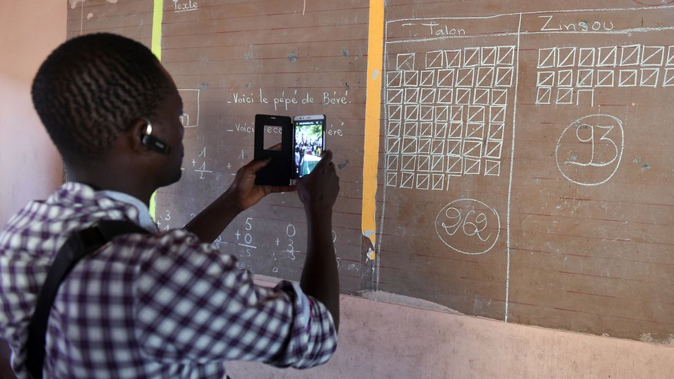 A man uses his phone to record the total votes cast in a polling station in Cotonou, Benin, 20 March 2024